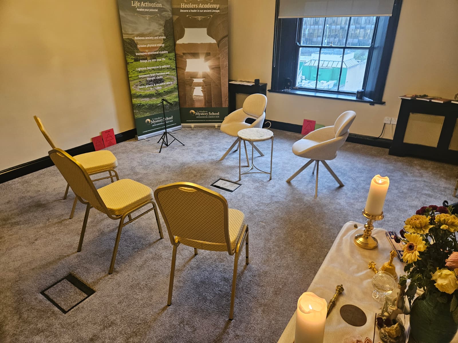 Èriu workshop room with chairs arranged around a central table, candles, flowers, and healing banners
